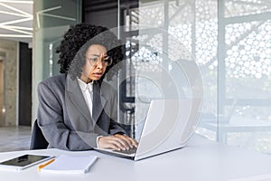 Worried young African American businesswoman working on laptop in office, looking upset at laptop screen