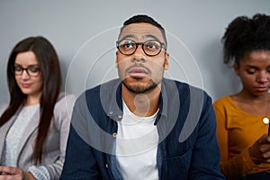 Worried young african american man expecting his turn for interview sitting with other female candidates