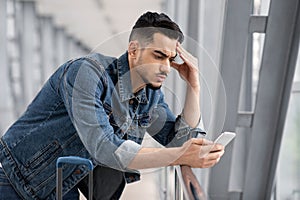 Worried young arab man looking at smartphone screen while waiting at airport