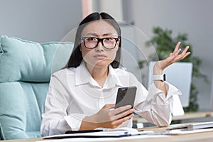 Worried young Asian business woman holds the phone in her hands,looks at the phone