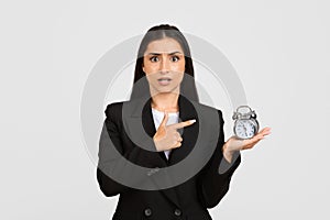 Worried young businesswoman pointing to clock