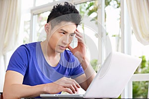 Worried Young Chinese Man Using Laptop At Home