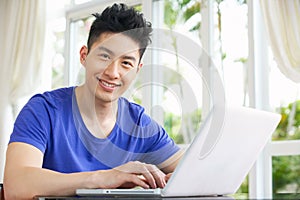 Worried Young Chinese Man Using Laptop At Home