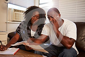 Worried Young Couple Sitting On Sofa Looking At Bills