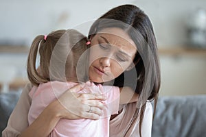 Worried young foster mother comforting embracing adopted child daughter photo