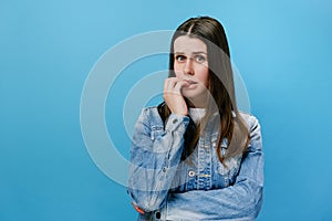 Worried young girl folded hands together near mouth, gnawing nails, young woman feels uncertain