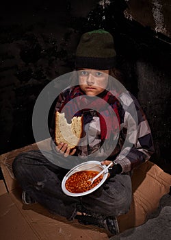 Worried young homeless boy eating charity food