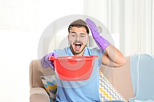 Worried young man collecting water leakage from ceiling at home.