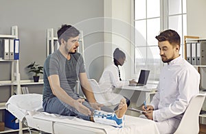 Worried young man with foot injury consulting doctor sitting on examination bed at clinic