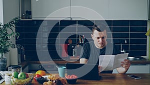 Worried young man paying bills online using laptop in the kithcen at home