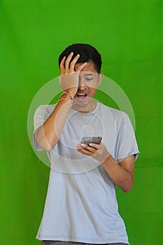 Worried young South Asian male looking down at his phone on green background