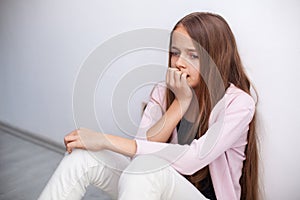 Worried young teenager girl sitting on the floor by the wall