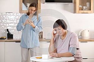 worried young woman calling doctor for her senior mother at home. sick senior woman with medication sitting at the table