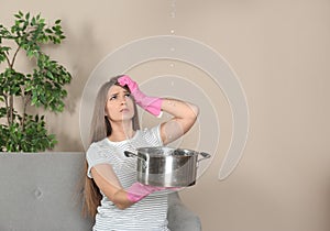 Worried young woman collecting water leakage from ceiling at home.