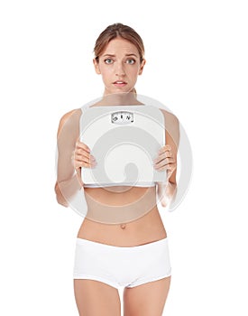 Worried young woman holding bathroom scales