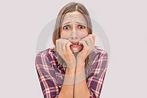 Worried young woman looks on camera. She is chewing fingers. Face is full of fear and different emotions. Isolated on