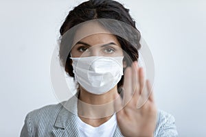 Worried young woman in protective facemask showing stop sign. photo