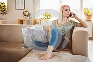 Worried young woman talking on mobile on sofa at home