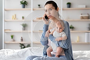 Worry Young Mother Holding Newborn Baby On hands And Talking On Cellphone