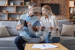 Worrying busy sad middle aged european lady with documents and male with tablet work with bills