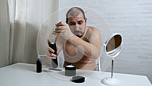 Worrying about hair loss.A balding man in front of a mirror takes care of his hair, uses a means for hair growth in case