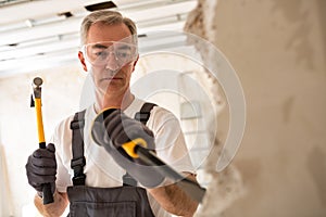 Worthy senior man working with hammer and tool while demolish wa