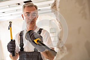 Worthy senior man working with hammer and tool while demolish wa photo