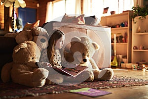 Would you like me to show you the pictures again. Shot of a little girl reading a book with her teddy bears around her.