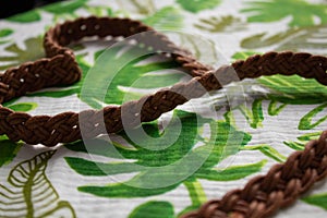 Woven brown belt as a heart on fabric painted with leaves. Front view