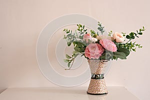 Woven vase with beautiful rose flowers on brown background. Copy space