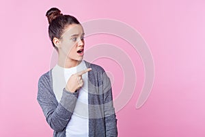 Wow, advertise here! Portrait of wondered teenage girl looking with open mouth in surprise, pointing to the side. pink background