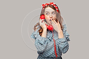 Wow! Amazed pinup girl holding phone handset surprised by conversation, covering her opened mouth shocked