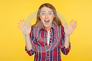 Wow, amazing news! Portrait of shocked pleased ginger girl in checkered shirt looking at camera with open mouth and surprised big