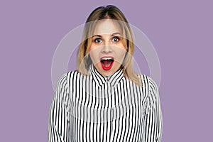 Wow amazing! Pleasantly surprised blond woman in striped blouse looking at camera with wide open mouth