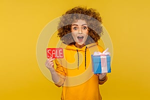 Wow, bonuses on Black Friday shopping! Portrait of surprised overjoyed curly-haired woman in urban style hoodie