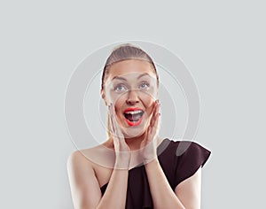 Wow. Closeup portrait young woman beautiful girl excited holding her mouth opened, hands on head looking up isolated on light blue