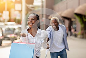 Wow, come with me to boutique. Happy woman with multicolored bags leads man to shopping