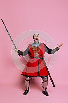 One young man, medieval warrior or knight wearing wearing armor clothing posing isolated over pink background