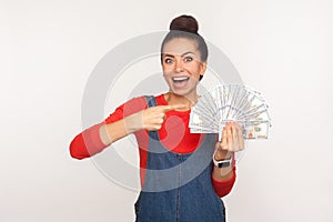 Wow, look at money, big profit! Portrait of shocked lottery winner, surprised rich girl with hair bun in denim overalls