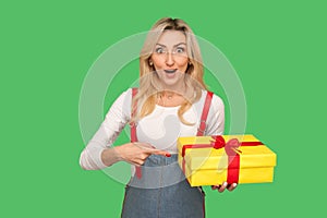 Wow, look at my gift! Portrait of surprised beautiful adult woman looking with amazement and pointing at wrapped box