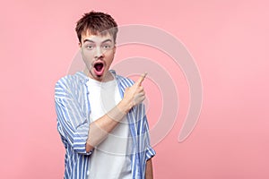 Wow shocking news! Portrait of amazed brown-haired man pointing at copy space for information, looking astonished. isolated on