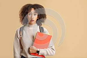 Wow, shocking news. Surprised african american woman with open mouth with backpack and smart watch holding notepads