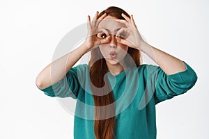 Wow super interesting promo. Excited redhead woman looking through finger binocular, seeing advertisement sale, spot