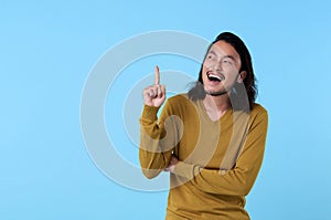 Wow and surprised young Asian man smiling with his finger pointing on blue background with copy space