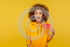 Wow, unbelievable shopping discount! Portrait of surprised curly-haired woman in urban style hoodie