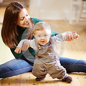 Wow, this walking thing is hard. Smiling young mom helping her baby boy learn to walk.