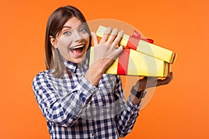 Wow, what a present! Portrait of young brunette woman with charming smile holding gift. isolated on orange background