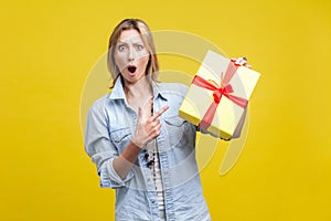 Wow, what a surprise! Portrait of amazed woman pointing at wrapped gift box. studio shot  on yellow photo