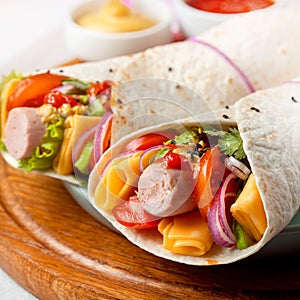 Wrap Homemade Tortilla with vegetables and cheese and organic sausage on a plate. wooden background.