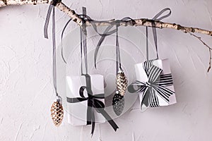 Wrapped black and white boxes with presents and decorative cones hanging on a branch